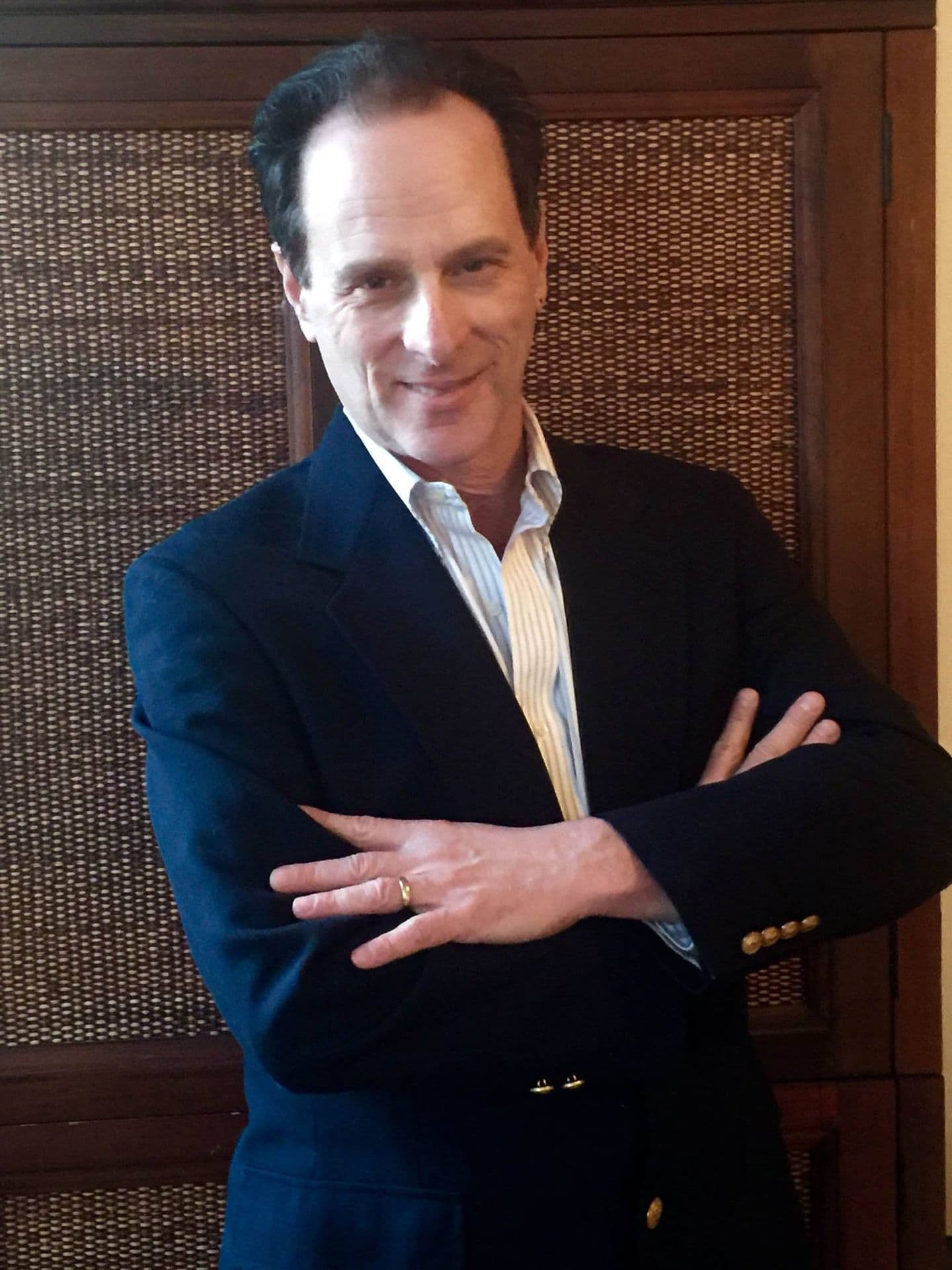 Smiling man in a navy blazer and striped shirt, standing with his arms crossed.