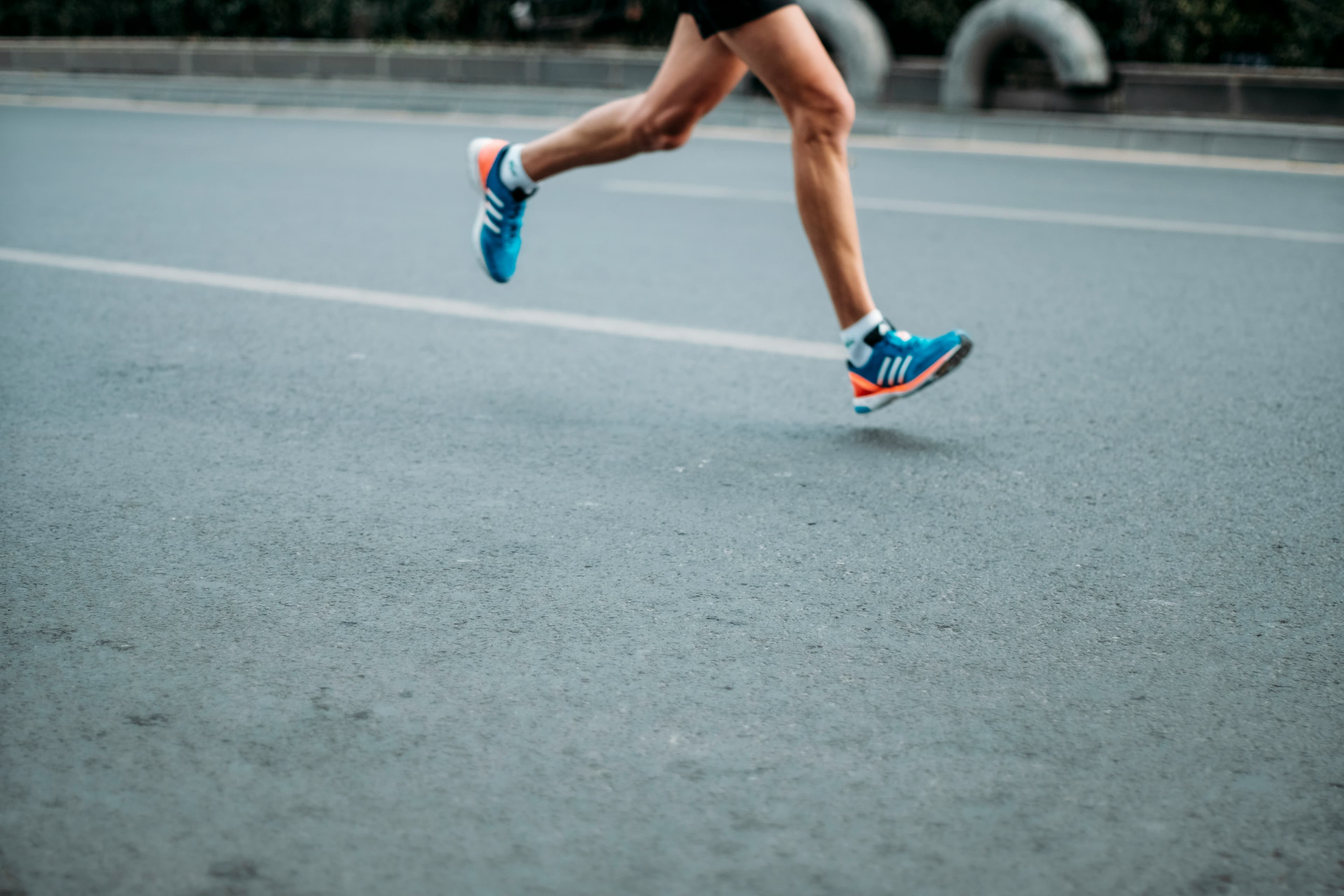 Close-up of a runner's legs and blue sneakers mid-stride on a paved city street.
